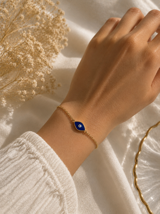 Blue enamel evil eye chain bracelet worn on a wrist beside dried flowers