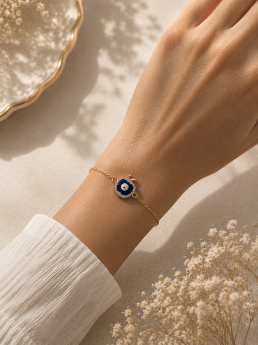 Gold-toned blue apple evil eye bracelet worn on the wrist against a soft sleeve