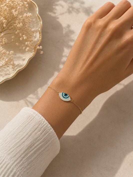 Gold-toned almond evil eye bracelet worn on the wrist with a white sleeve