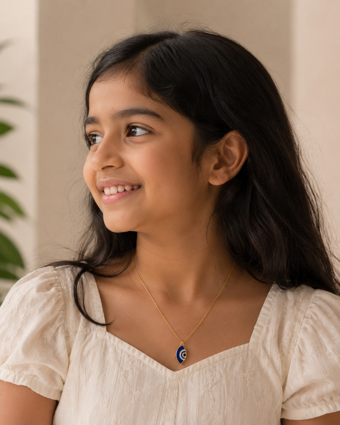 Model in cream top wearing the blue marquise evil eye pendant on a gold-toned chain