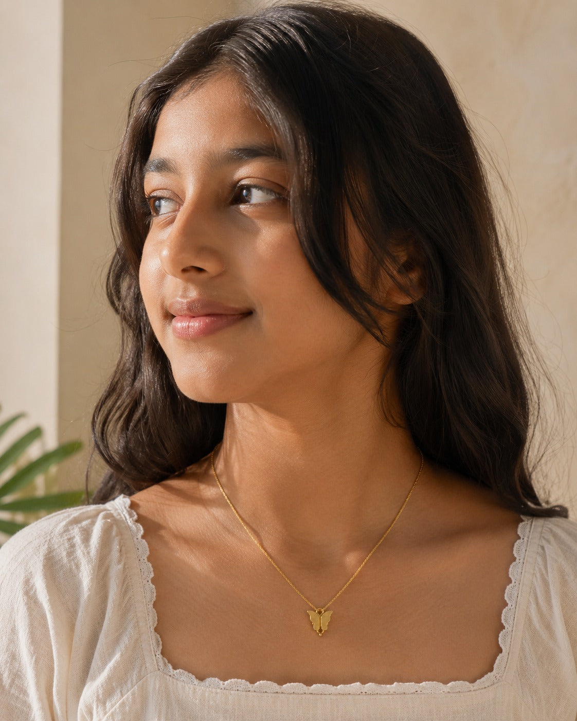 Model wearing the gold-toned butterfly pendant on a fine chain with a cream neckline