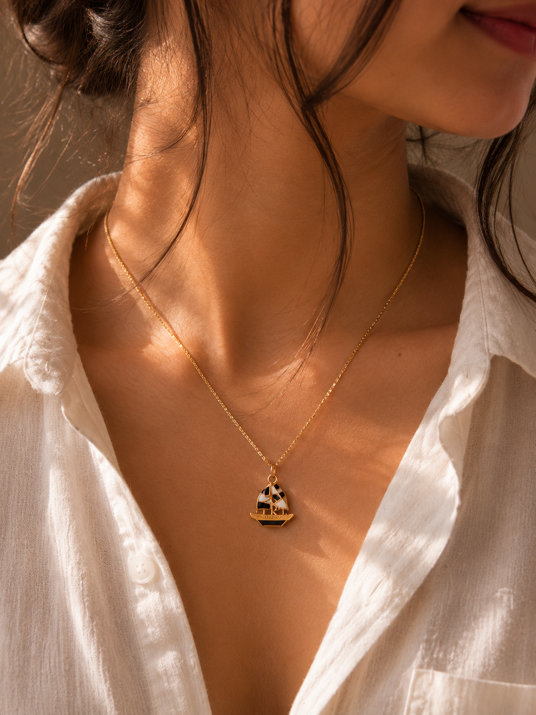 Close view of the gold-toned sailboat enamel pendant worn on a chain over a white shirt