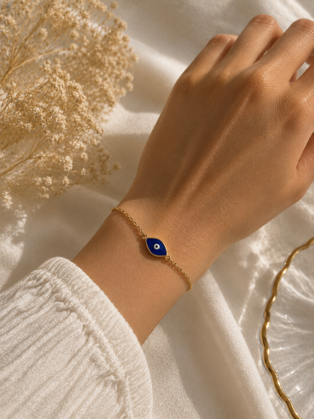 Blue enamel evil eye chain bracelet worn on a wrist beside dried flowers