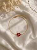 Gold-toned chain bracelet with a red enamel heart evil eye charm on cream satin