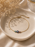 Gold-toned chain bracelet with three green, blue and red enamel evil eye charms on a ceramic dish