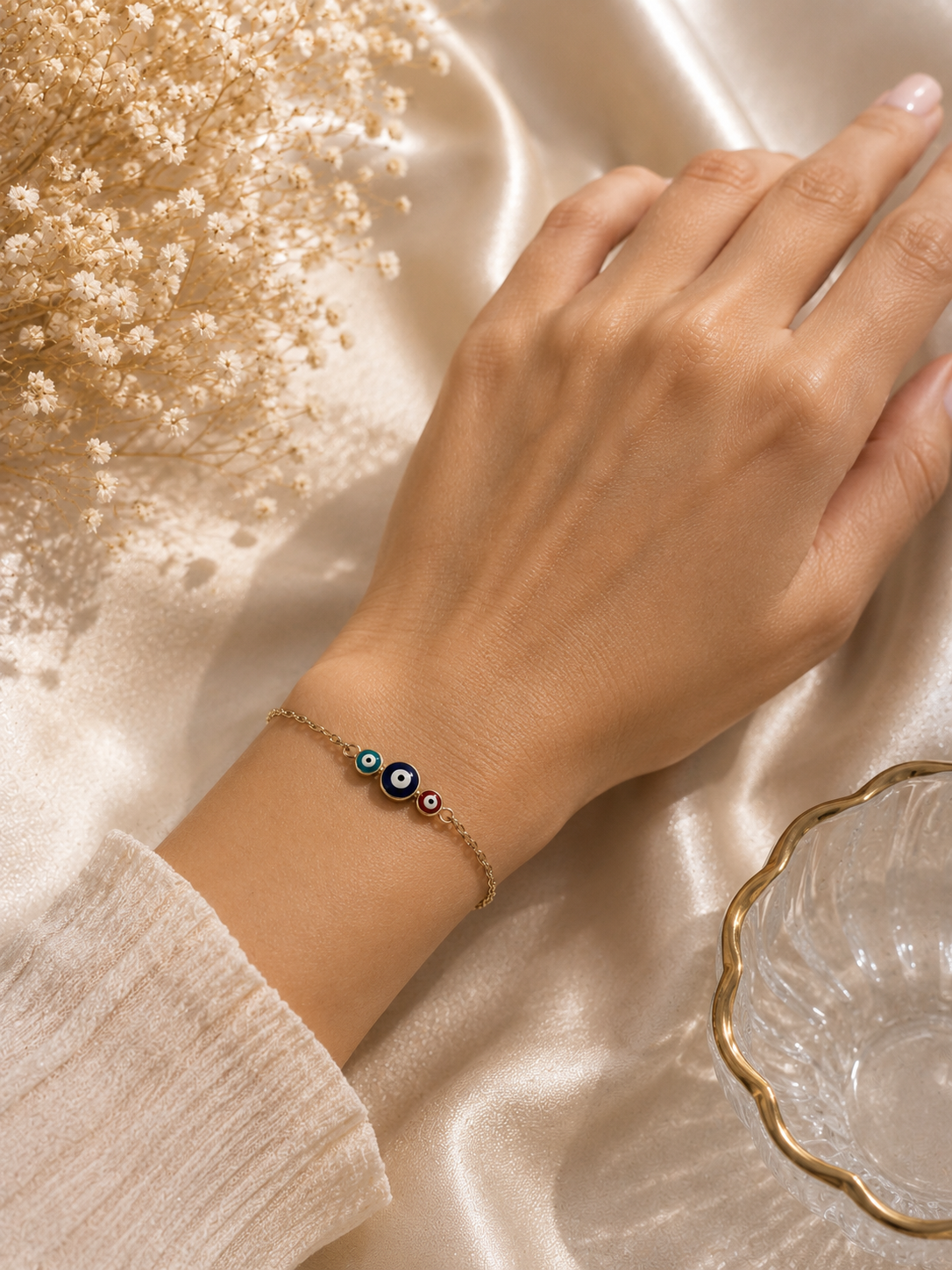 Triple evil eye multicolour charm bracelet worn on a wrist over cream fabric