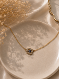 Gold-toned chain bracelet with a crystal halo evil eye charm on a ceramic dish