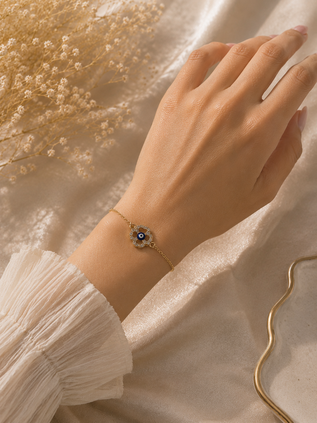 Crystal halo evil eye bracelet worn on a wrist beside dried flowers