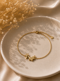 Gold-toned giraffe charm bracelet on a fine chain styled on a cream plate with dried flowers