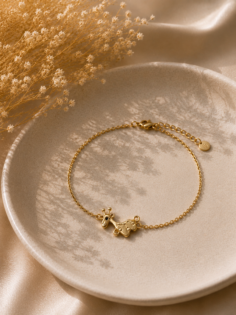 Gold-toned giraffe charm bracelet on a fine chain styled on a cream plate with dried flowers