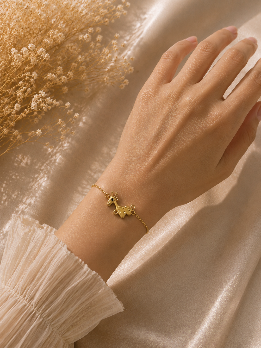 Gold-toned giraffe charm bracelet worn on the wrist with a soft ivory sleeve