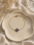 Gold-toned bracelet with a blue enamel apple evil eye charm on a scalloped cream dish