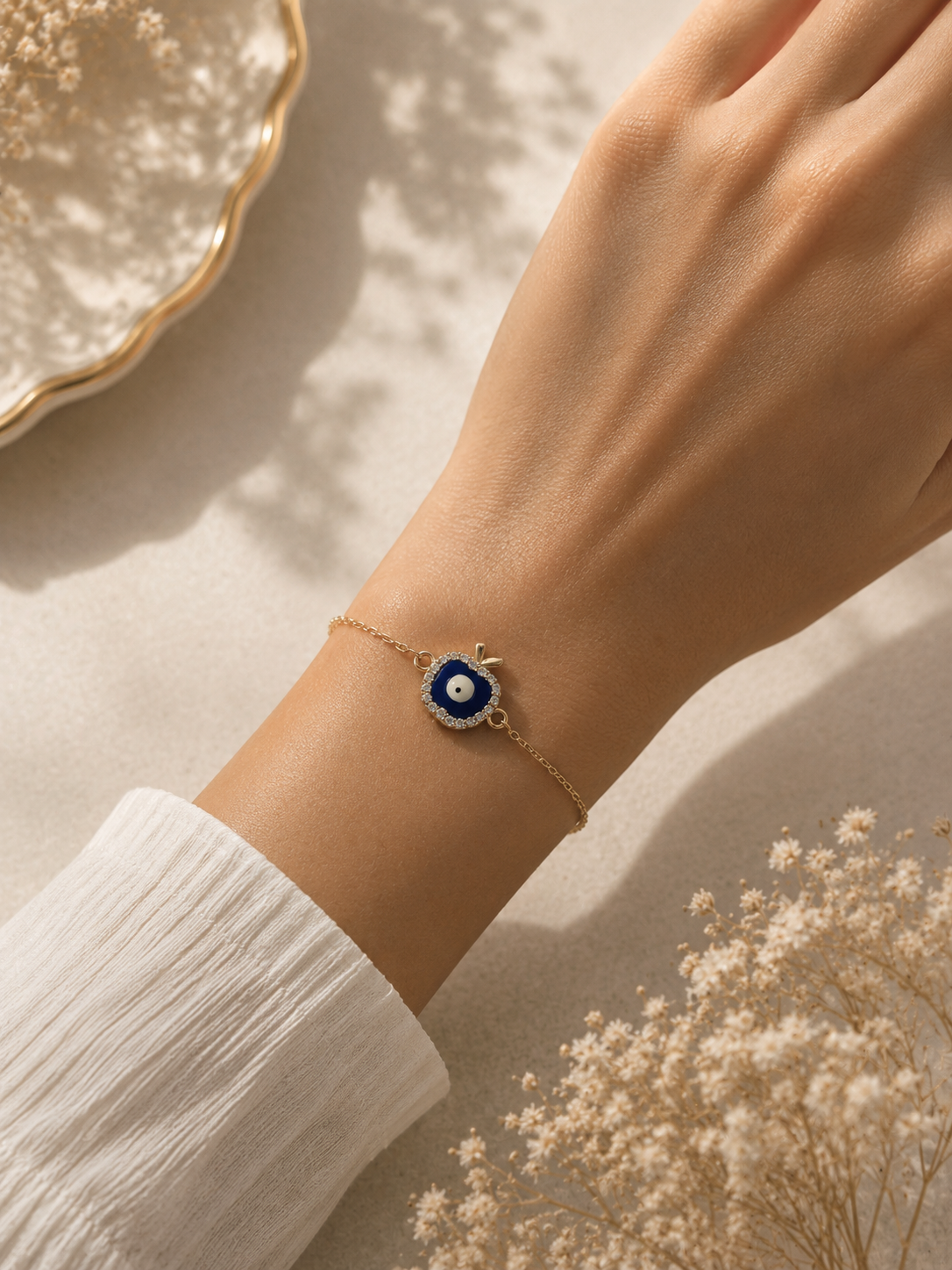 Gold-toned blue apple evil eye bracelet worn on the wrist against a soft sleeve