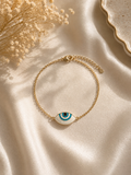 Gold-toned bracelet with an almond-shaped enamel evil eye charm on ivory satin