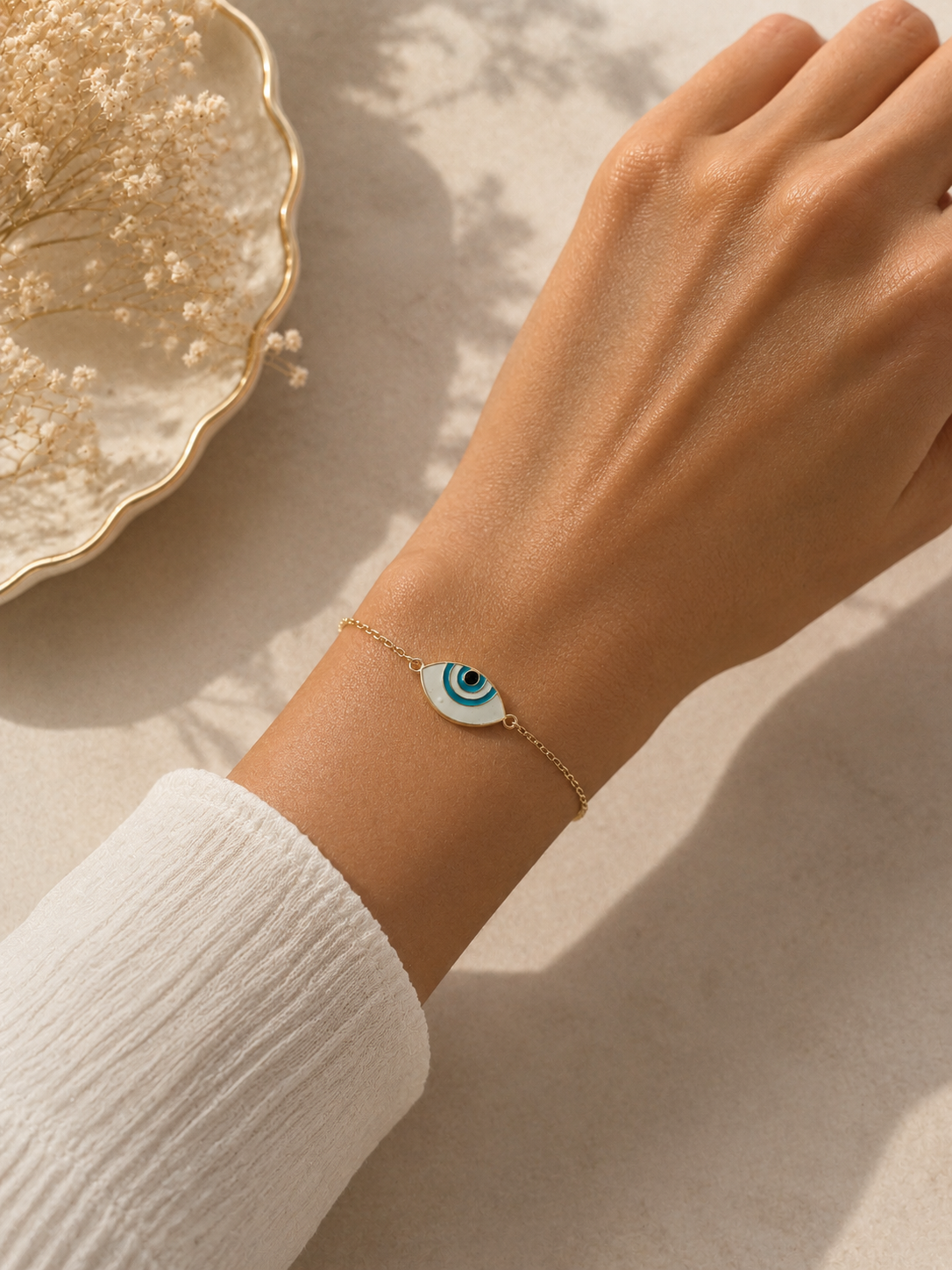 Gold-toned almond evil eye bracelet worn on the wrist with a white sleeve