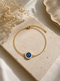 Gold-toned bracelet with a round enamel evil eye charm resting on a textured stone block