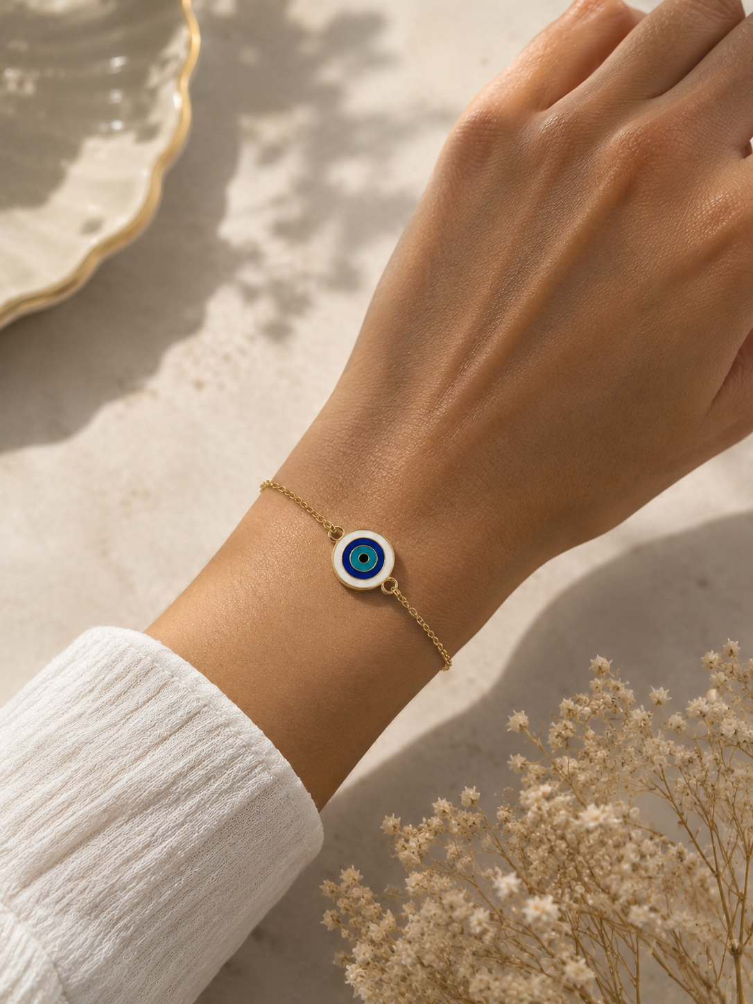 Gold-toned round evil eye bracelet worn on the wrist with a white sleeve