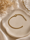 Gold-toned woven curb chain bracelet arranged on a cream plate with dried flowers