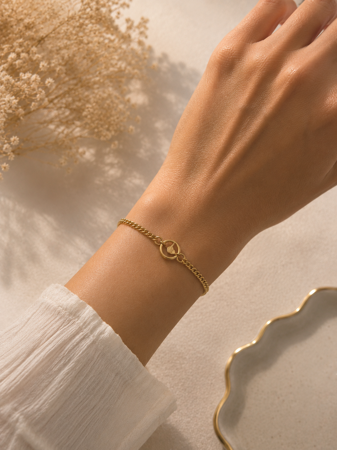 Gold-toned woven curb chain bracelet worn on the wrist with a white sleeve