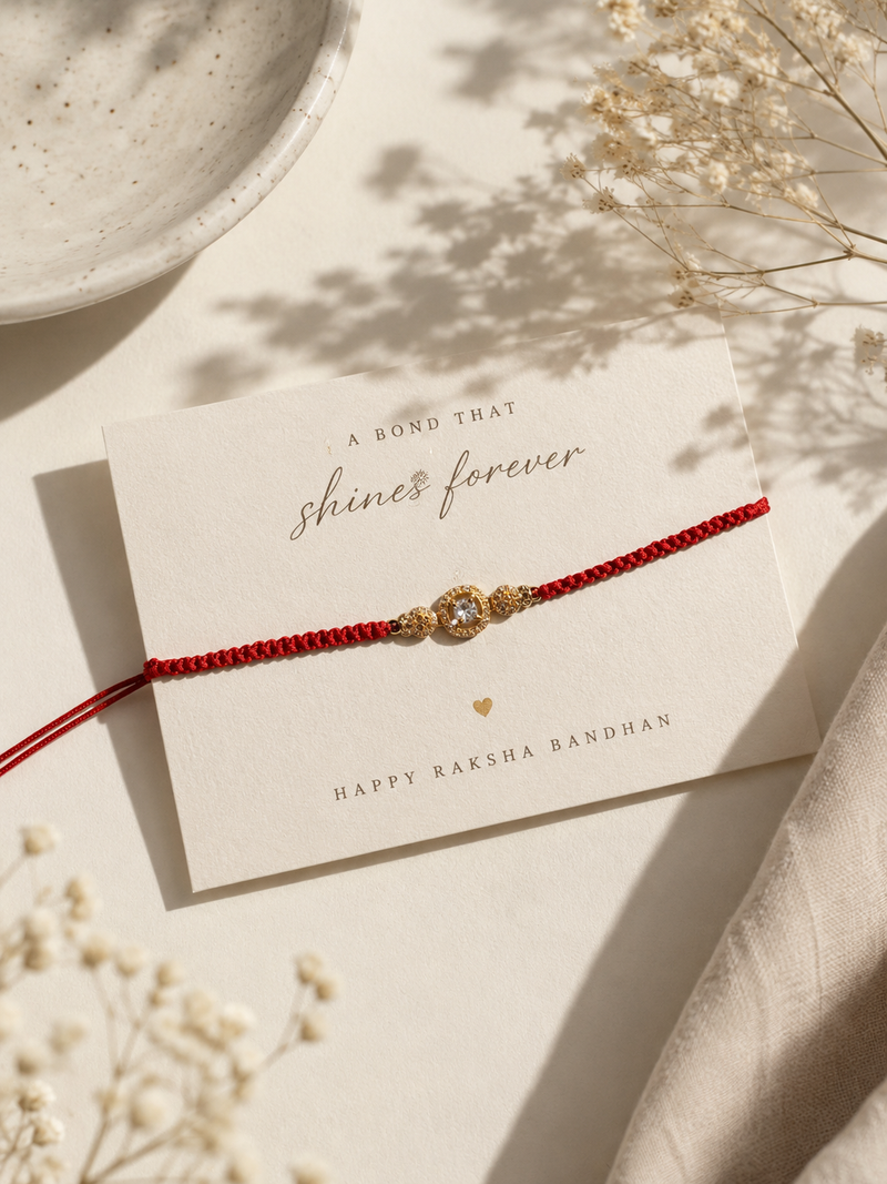 Gold three-stone rakhi on a red thread on a bond that shines forever card