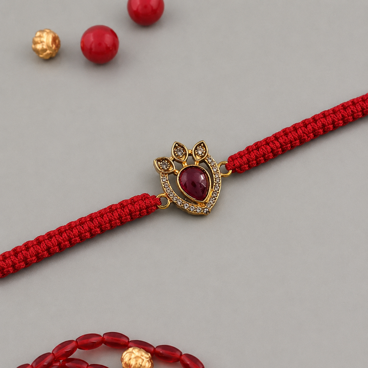 Gold crown motif rakhi with a red teardrop stone on a red thread, on a wooden table with puja bowls