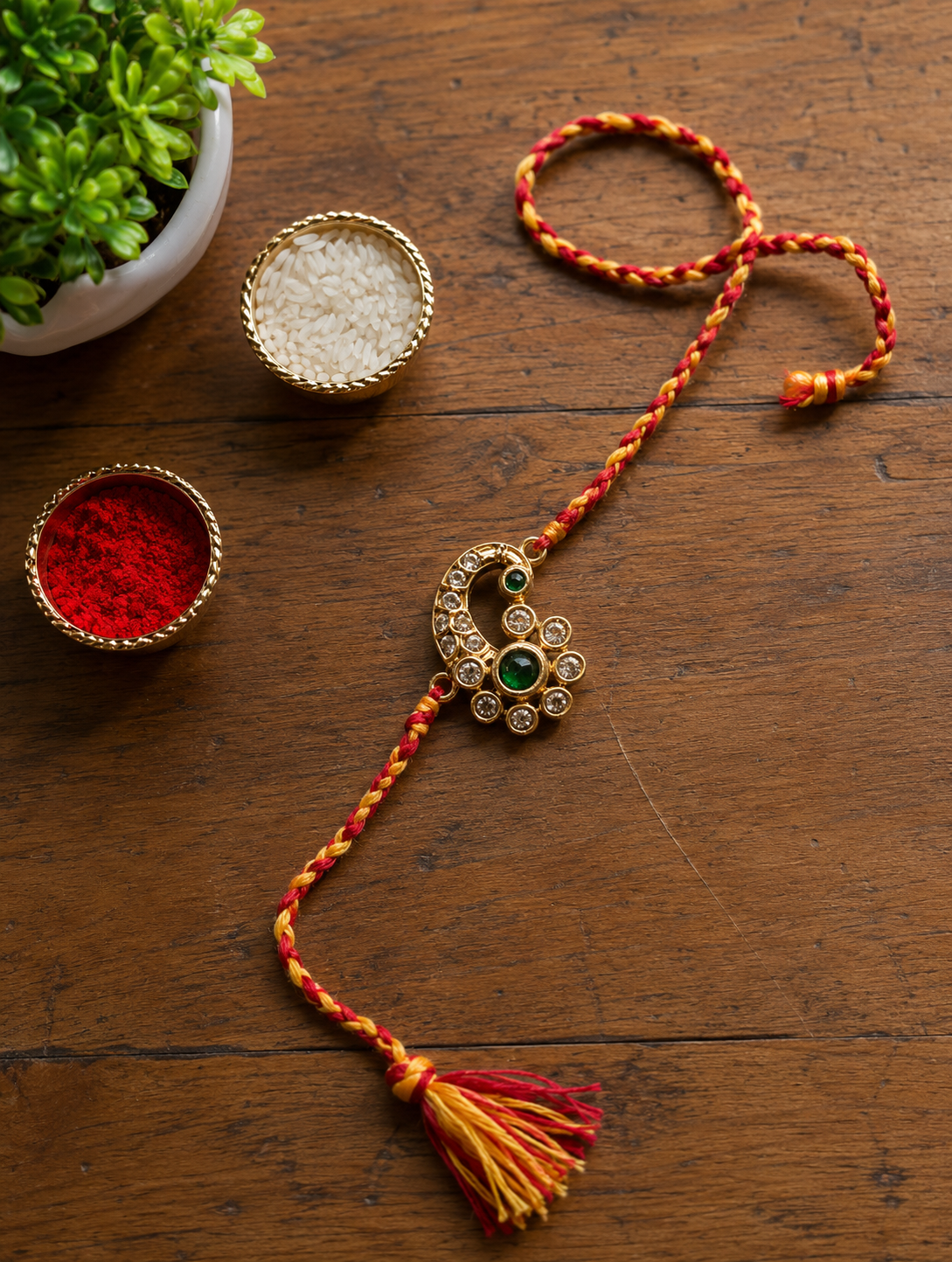 Gold paisley lumba rakhi with a green stone and tassel on a red and yellow thread