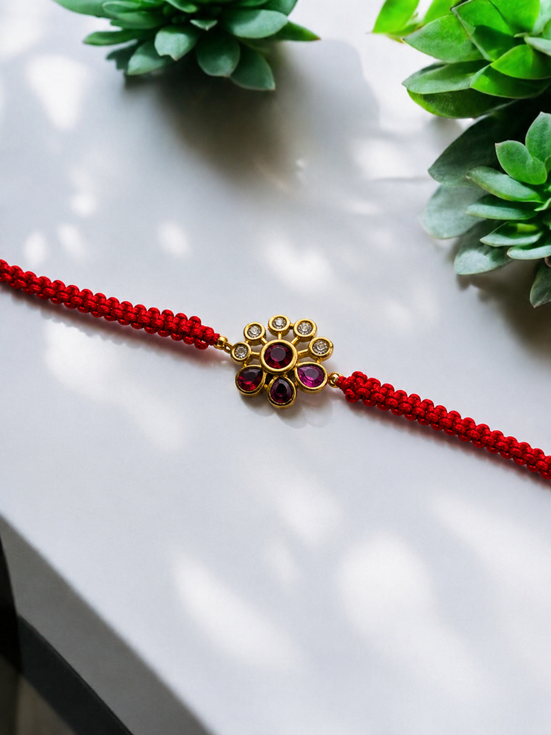 Gold petite floral kundan rakhi with red stones on a finely beaded red thread