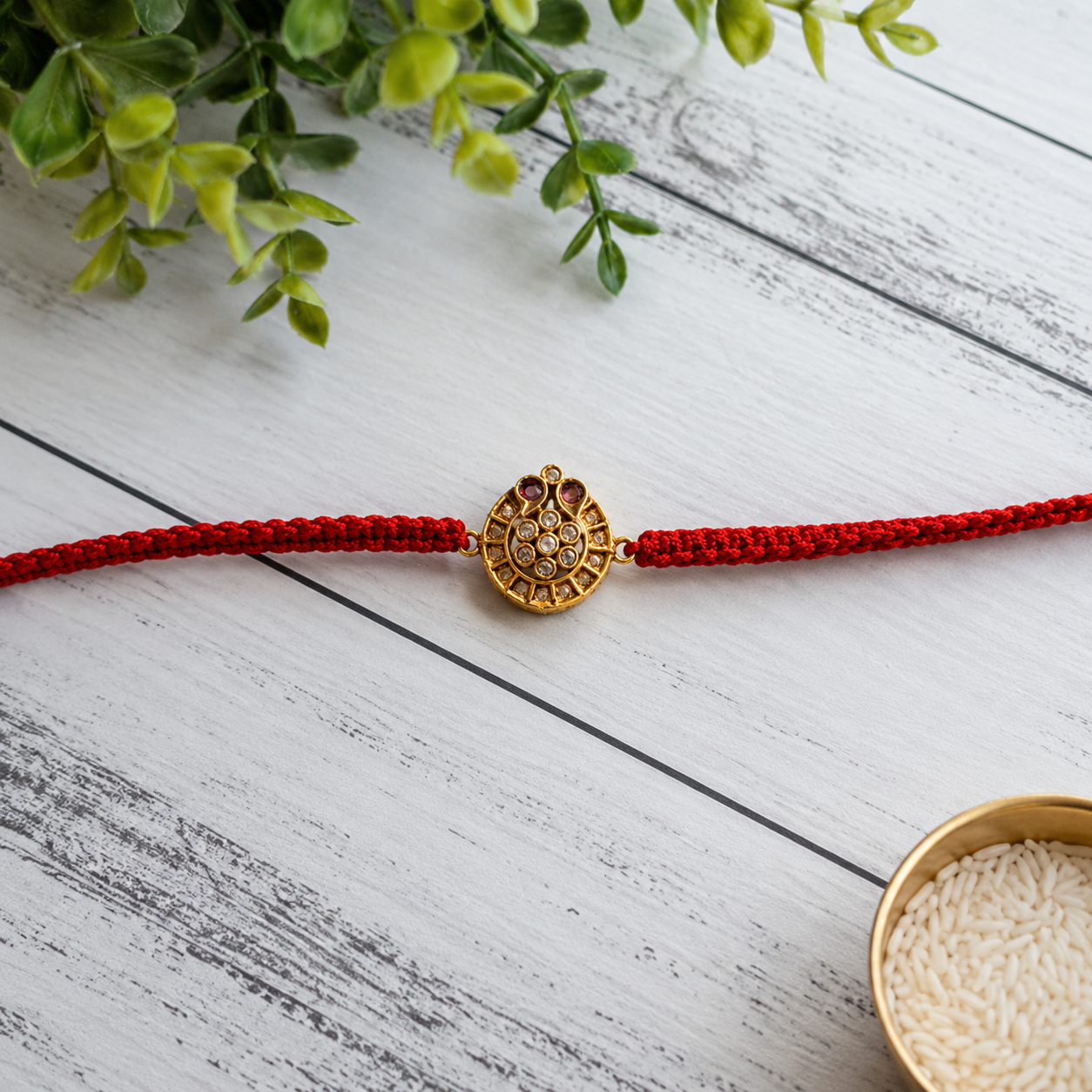 Gold antique round disc rakhi on a red thread on a white wooden surface with greenery