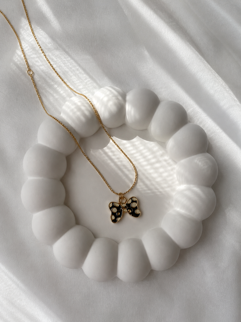 Gold-toned butterfly pendant necklace with black spotted enamel laid flat on a white surface