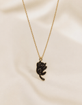 Gold-toned necklace with a black enamel climbing cat pendant on a cream surface