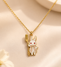Gold-toned necklace with a white enamel bunny pendant holding a fork on a soft pink surface