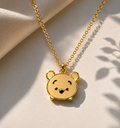 Polished gold-toned teddy bear face pendant on a fine chain over cream fabric