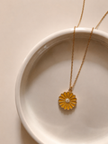Gold-toned rope chain with a mustard-yellow enamel daisy pendant on a white plate