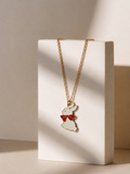 White enamel bunny pendant with red bow on a gold-toned chain displayed on a cream block