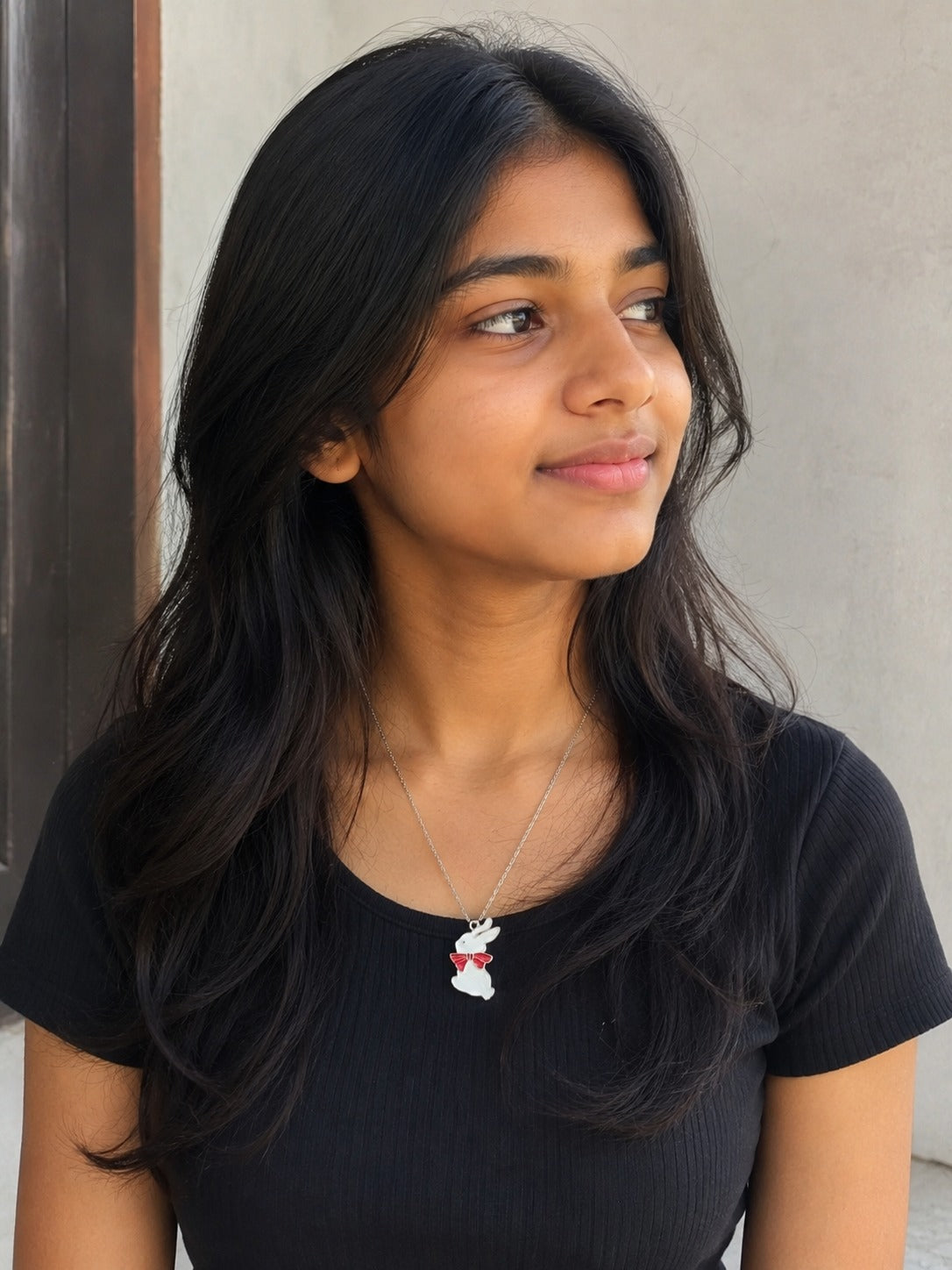 Model wearing the white enamel bunny pendant with red bow on a fine chain