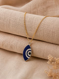 Blue and white marquise evil eye enamel pendant on a gold-toned chain resting on linen