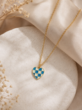 Blue and cream checkerboard enamel heart pendant on a gold-toned chain on a stone dish