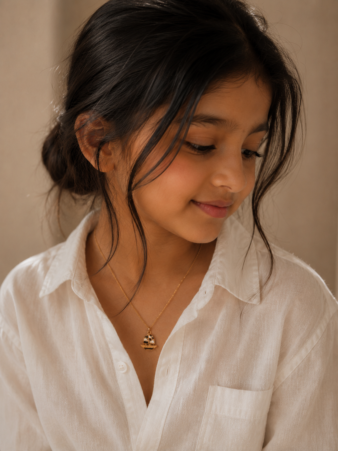 Model in a white shirt wearing the gold-toned sailboat pendant on a fine chain
