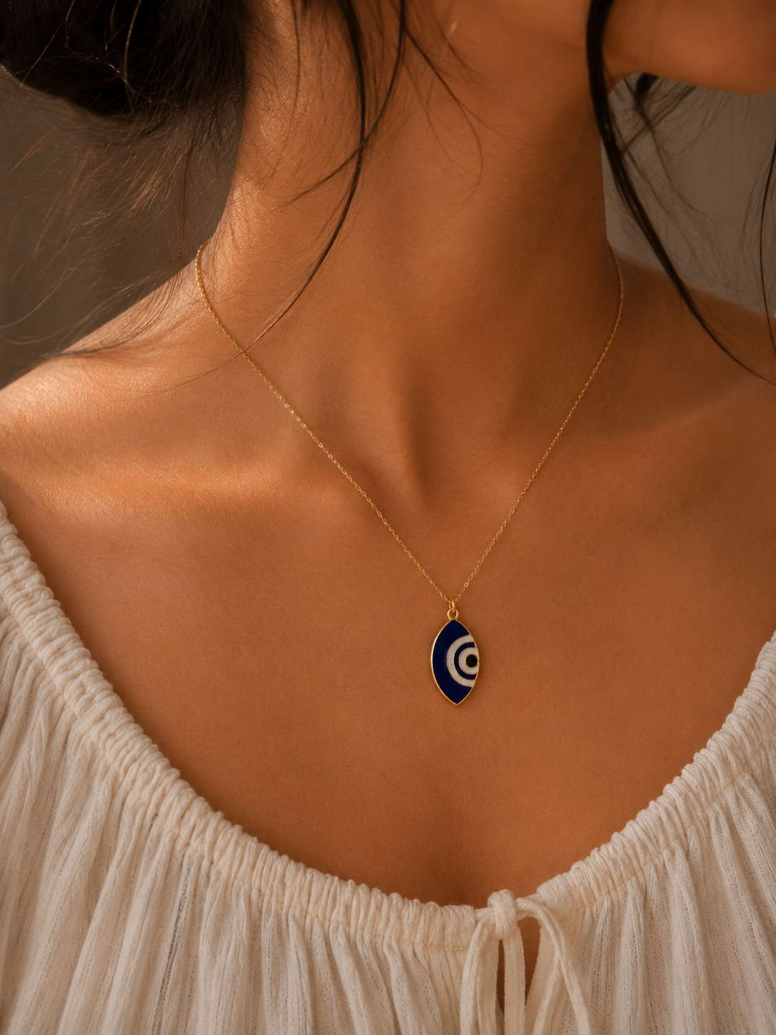 Model wearing the cobalt evil eye marquise pendant on a fine gold-toned chain over a cream top