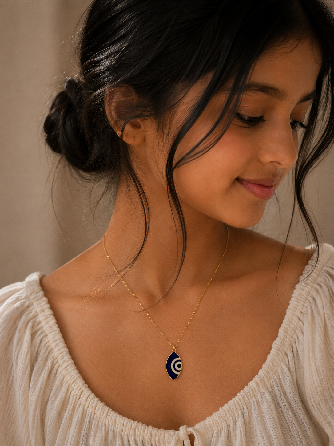 Model in a cream top wearing the blue marquise evil eye pendant on a gold-toned chain