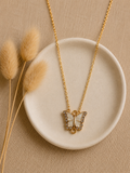 Gold-toned butterfly pendant necklace with white enamel and crystal wings on a trinket dish