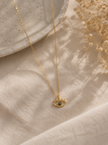 Gold-toned evil eye pendant necklace with blue centre stone on neutral fabric