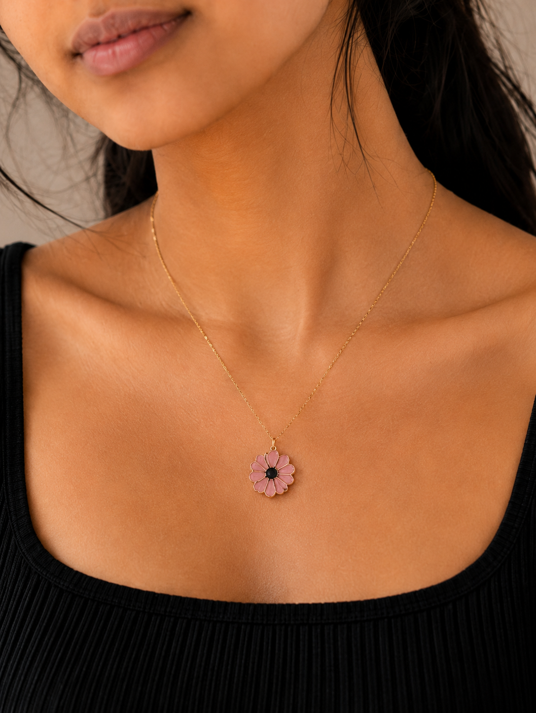 Pink daisy pendant necklace worn close-up against a black top