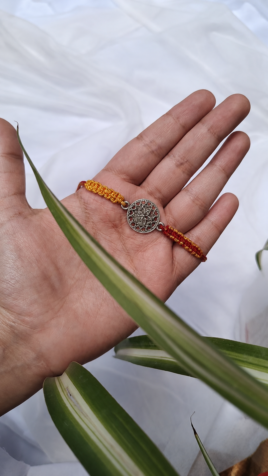 Silver filigree coin rakhi on a saffron beaded thread held in hand