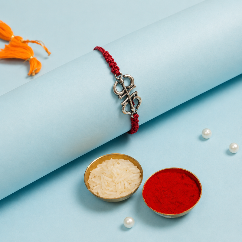 Ornamental silver Om rakhi on a red braided thread on ivory satin