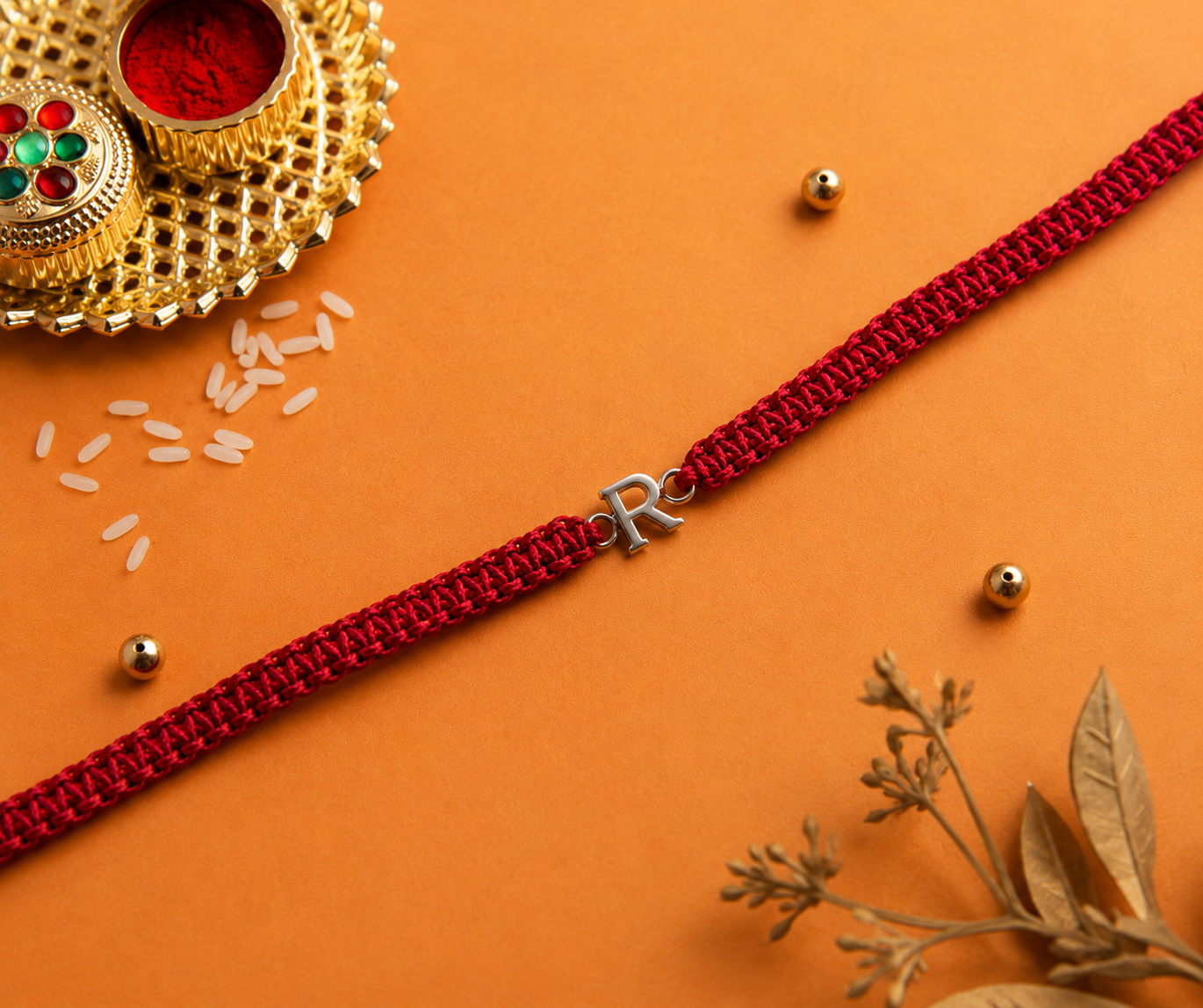 Silver initial R red thread rakhi flat lay