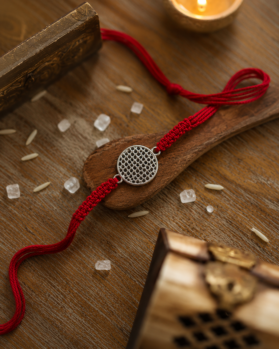 Silver jaali lattice disc rakhi on a red thread on a wooden surface