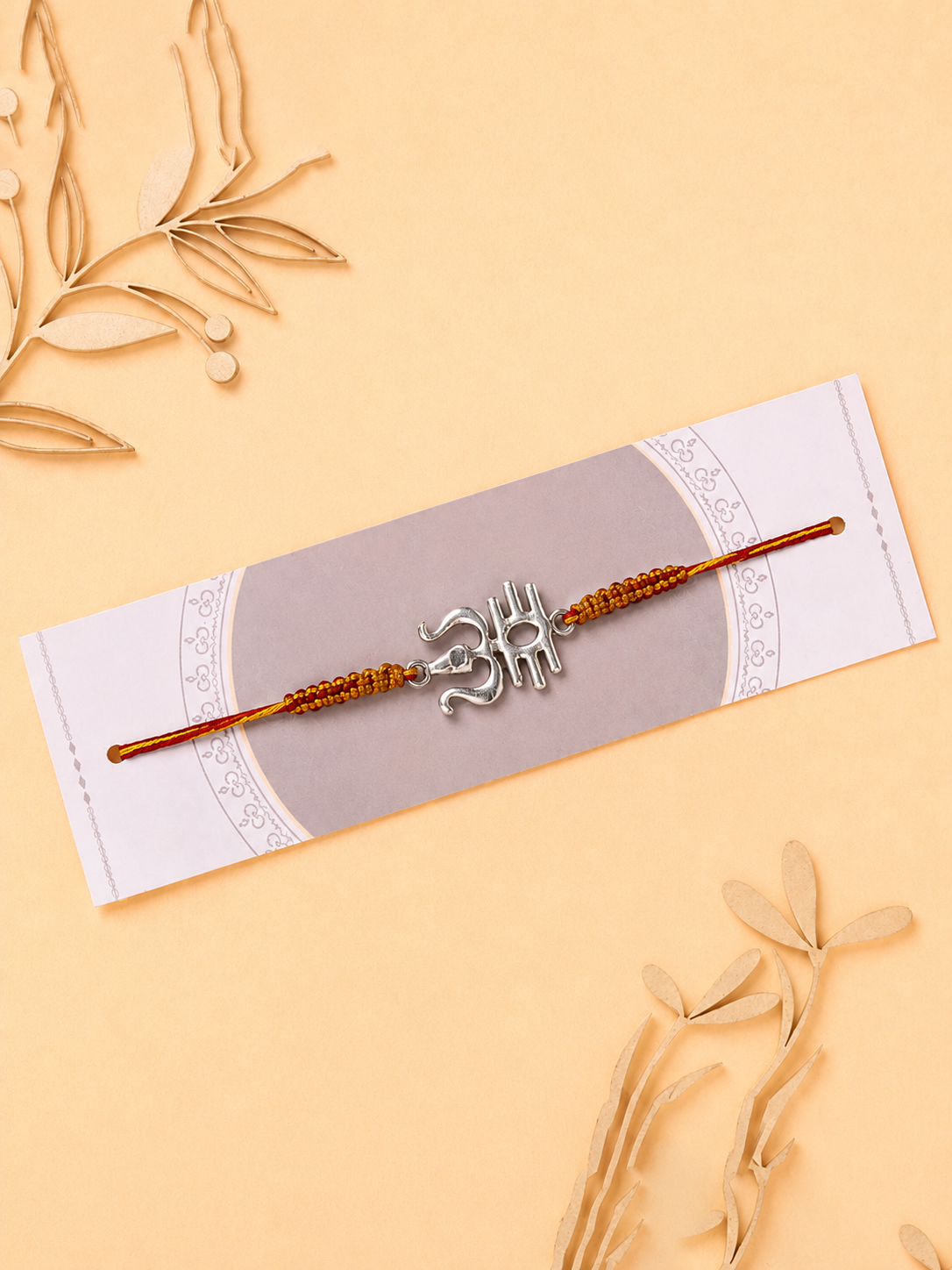Silver calligraphic Om rakhi on a saffron beaded thread on a card